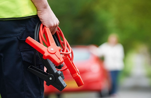 man holding jump leads approaching broken down vehicle