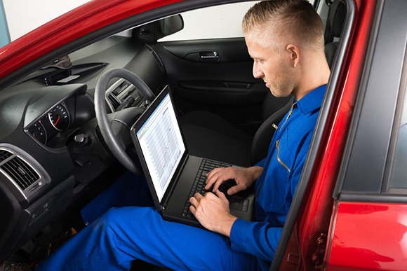 technician sitting in red car on laptop