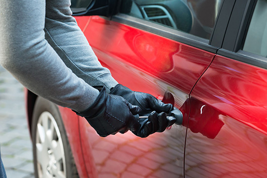 man breaking into red car