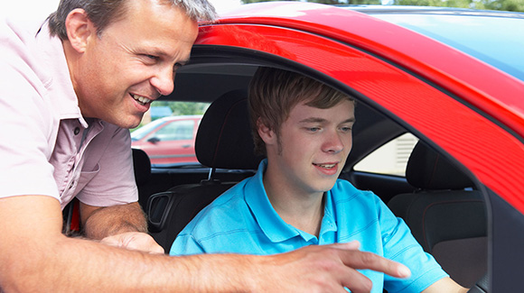teenage boy learning to driver with instructor showing car controls
