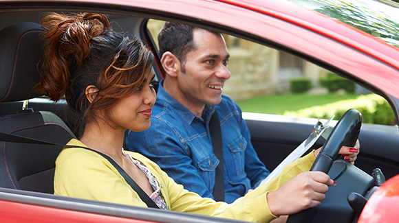 young female learner driver having driving lessons with young professional driving instructor