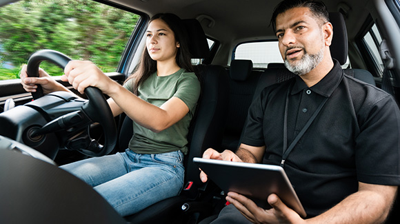 young lady learning to drive with driving instructor