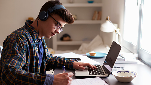 teenage boy wearing headphones revising in his bedroom