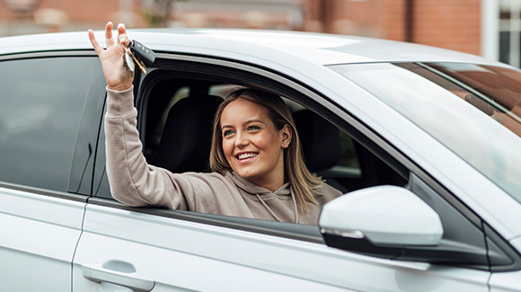 happy young lady just passed driving test holding up car keys out of window