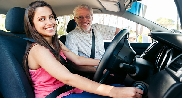 happy young lady in car learning to drive with driving instructor 