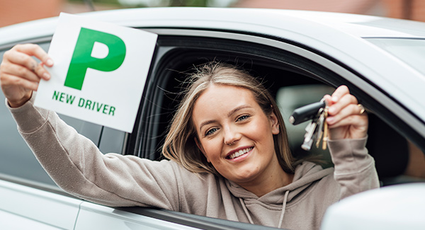 Happy young lady leaning out of car window holding a p plate after passing driving test